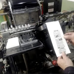 mano sujetando una impresión tipográfica delante de una máquina de impresión